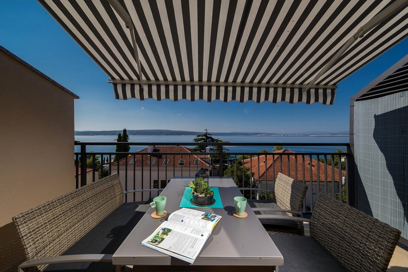 Tavolo del balcone sotto una tenda da sole a righe con vista sul mare
