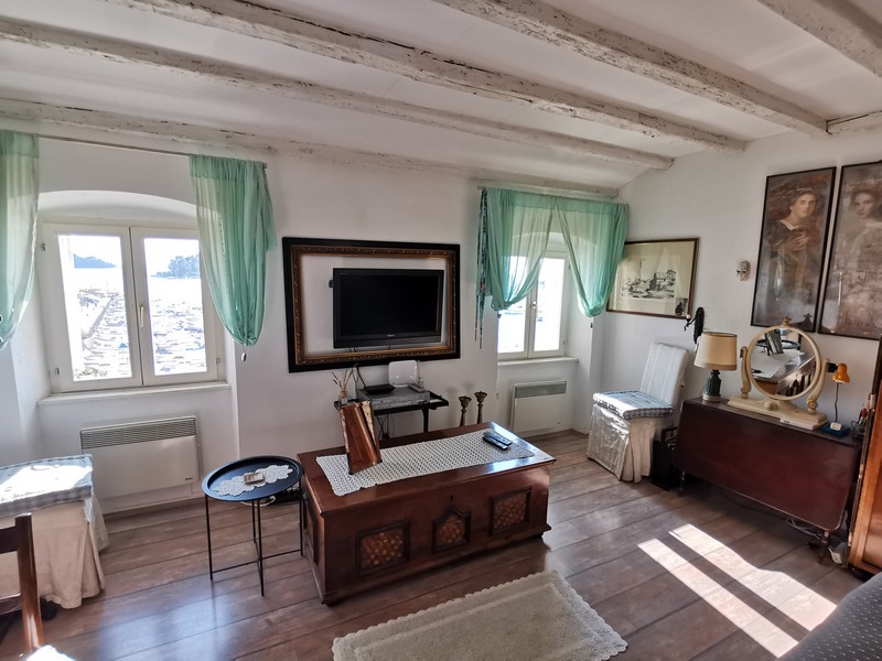 Soggiorno con soffitto a travi di legno e cassapanca davanti alle finestre ad arco