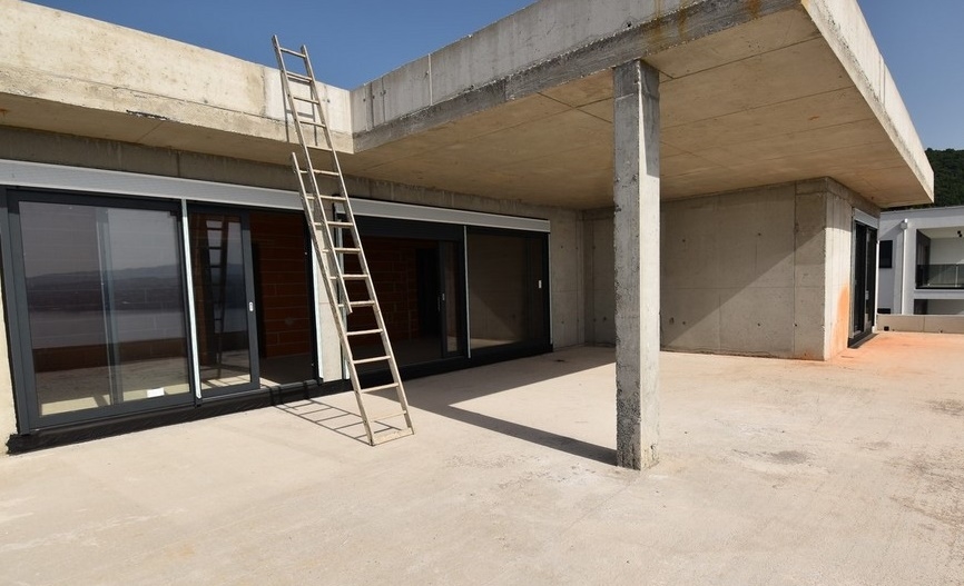 Struttura al grezzo con pilastri in cemento e scala a pioli sulla terrazza