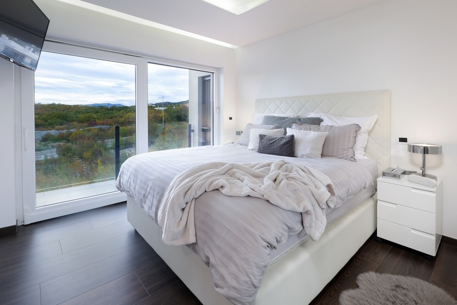 Camera da letto in bianco con finestra a tutta altezza sul verde