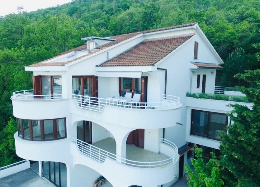 Casa bianca con balconi rotondi davanti al pendio boscoso