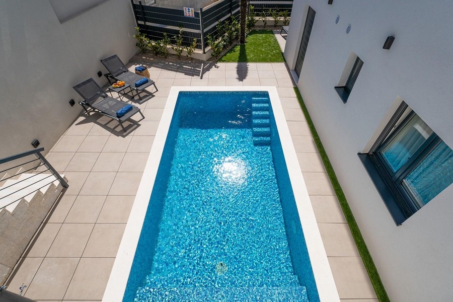 Piscina con lettini vista dall'alto tra il muro della casa e la recinzione
