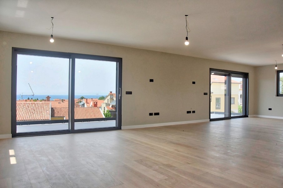 Ampio interno non arredato di un attico in vendita in Istria con vista mare attraverso grandi finestre.