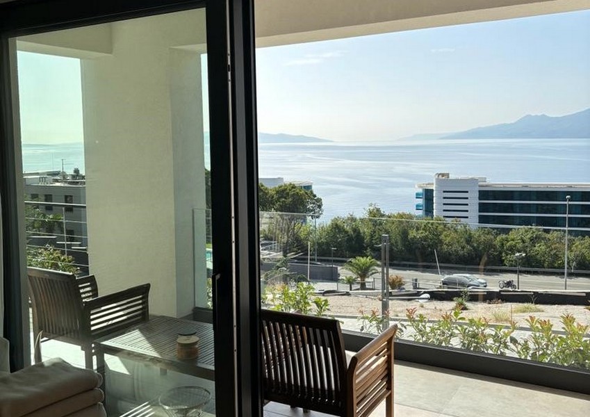 Balcone con sedie in legno e vista mare attraverso una porta di vetro aperta, offerta immobiliare a Rijeka, Croazia.