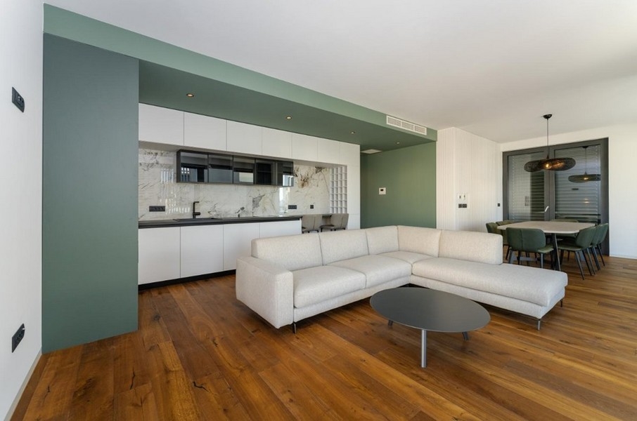 Soggiorno aperto con cucina, pavimento in legno e parete verde