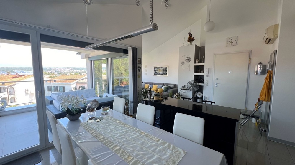 Zona pranzo e cucina con mobili moderni, ampia vetrata verso la terrazza con vista mare.
