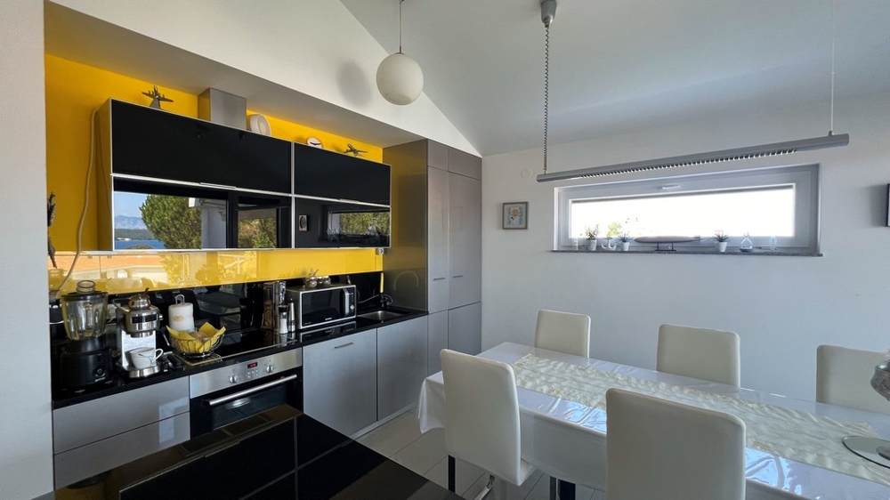 Cucina moderna con piano di lavoro nero e parete di fondo gialla, zona pranzo adiacente.
