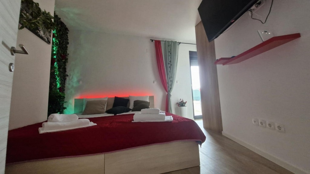 Camera da letto con copriletto rosso, sfondo decorativo e televisore a parete