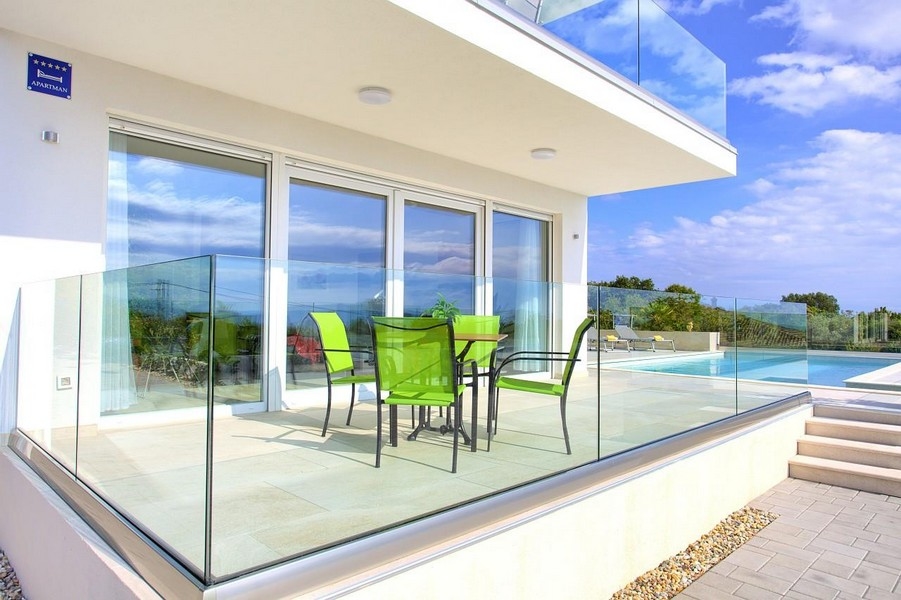Terrazza con sedie verdi e parapetto in vetro accanto alla piscina