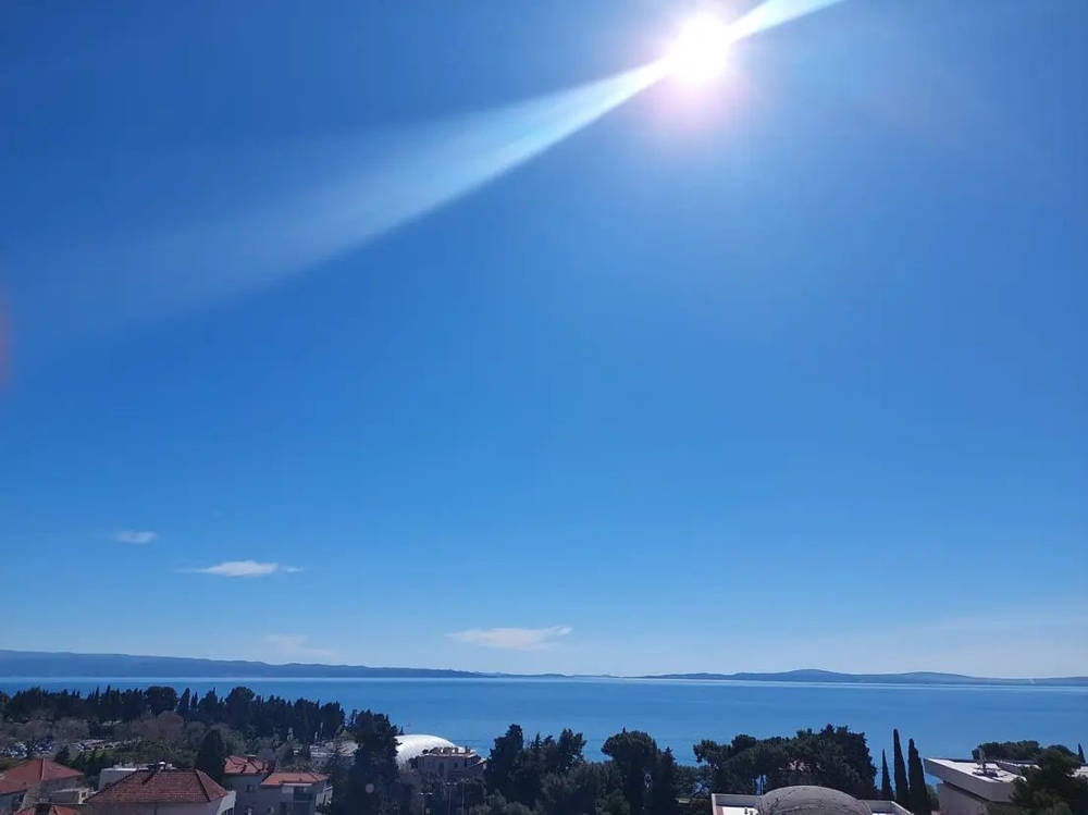 Sole sulla baia con cipressi e tetti sullo sfondo