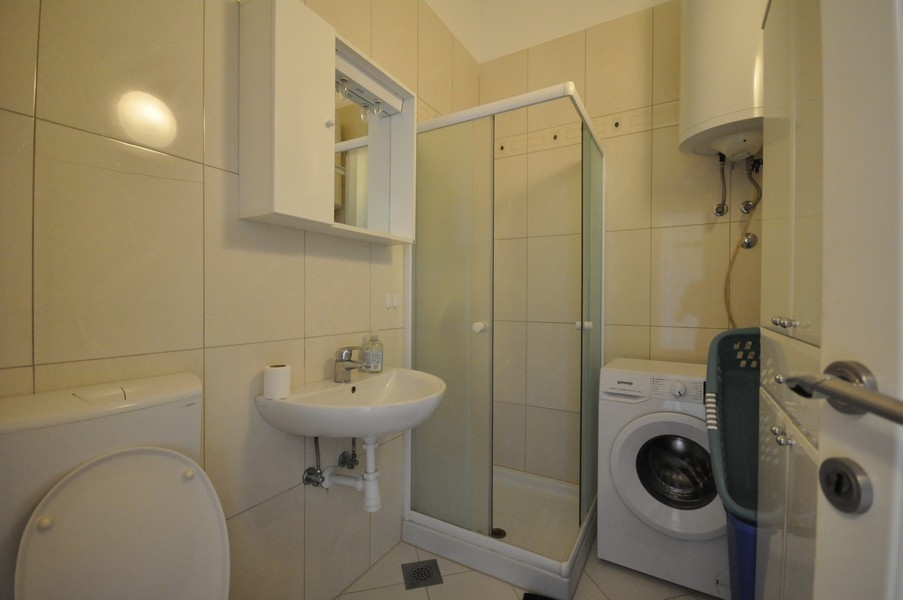 Bagno con doccia, lavabo, WC e lavatrice, pareti e pavimento con piastrelle chiare
