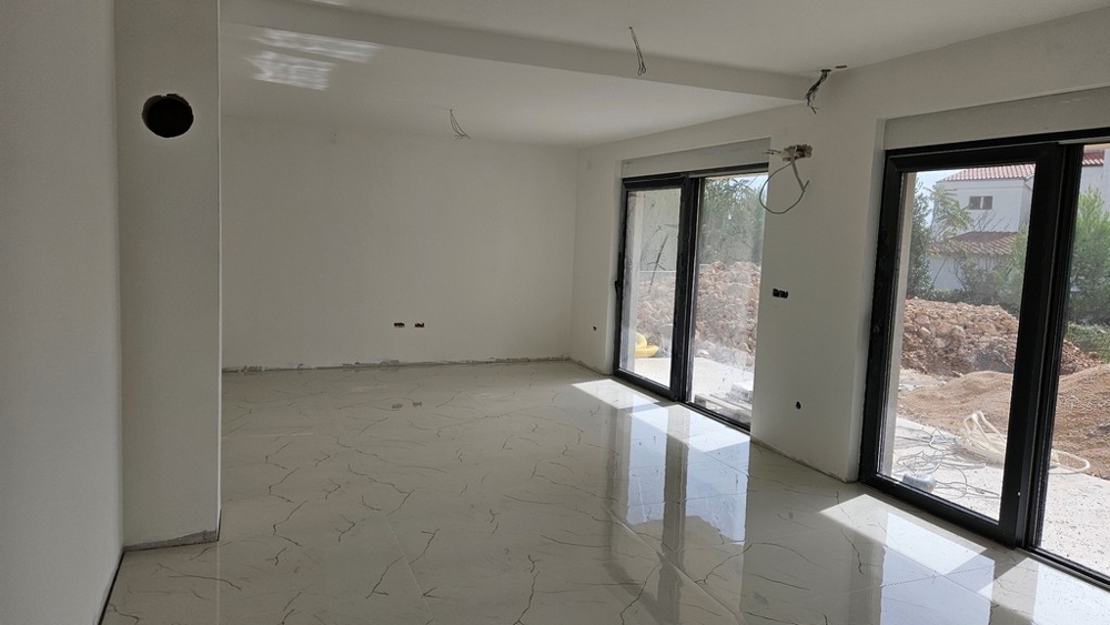 Interno con grande superficie finestrata, pareti bianche e pavimento piastrellato, ancora in costruzione.