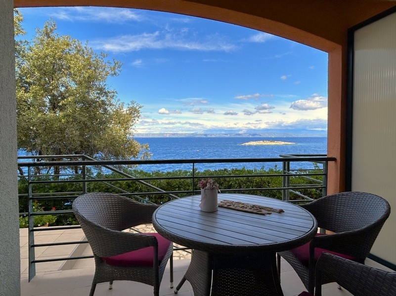 Tavolo sul balcone con sedie in vimini e vista sulla piccola isola