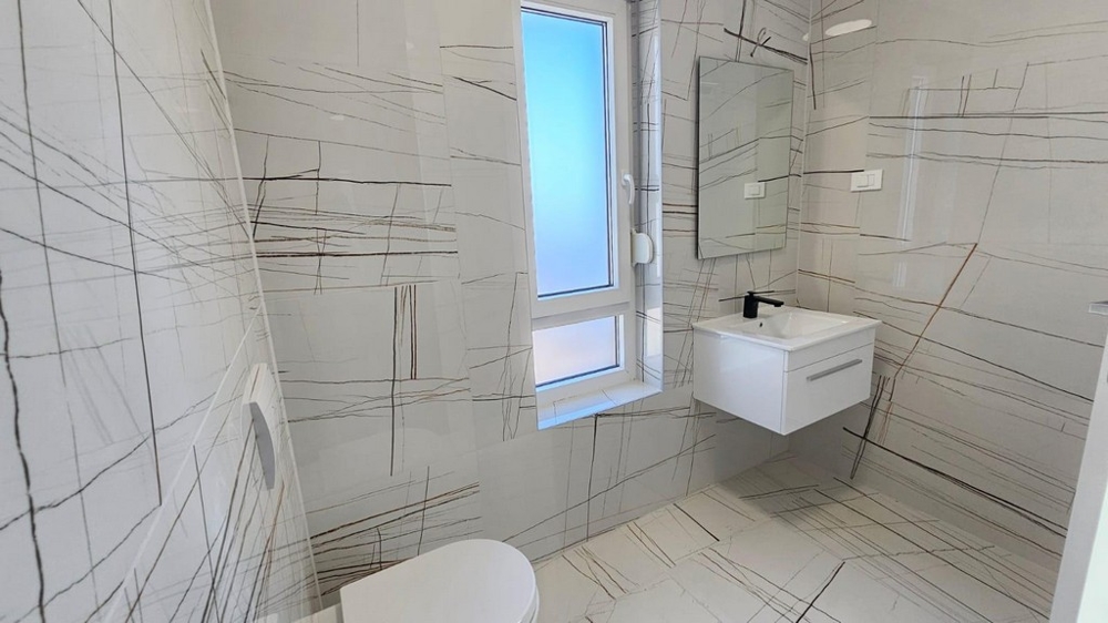 Bagno con piastrelle moderne, finestra, lavabo e WC