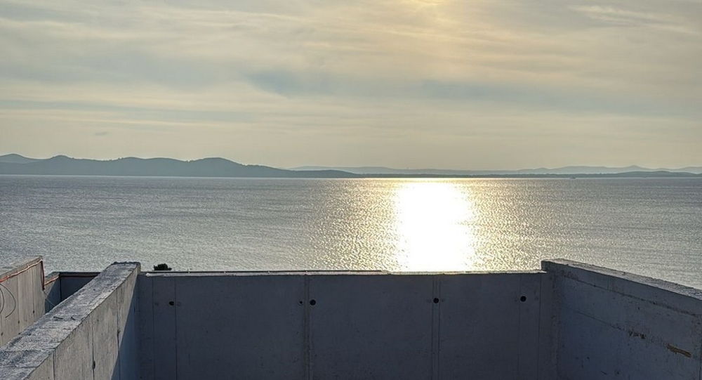 Riflesso del sole sull'acqua dietro il parapetto in cemento