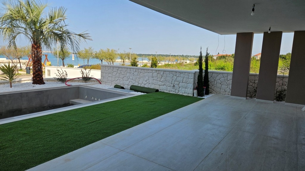 Terrazza con erba sintetica e palma davanti al muro in pietra naturale