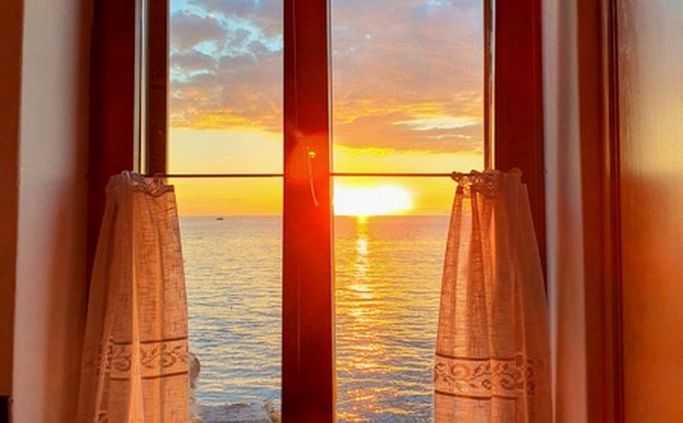 Sole della sera sul mare dietro la finestra in legno