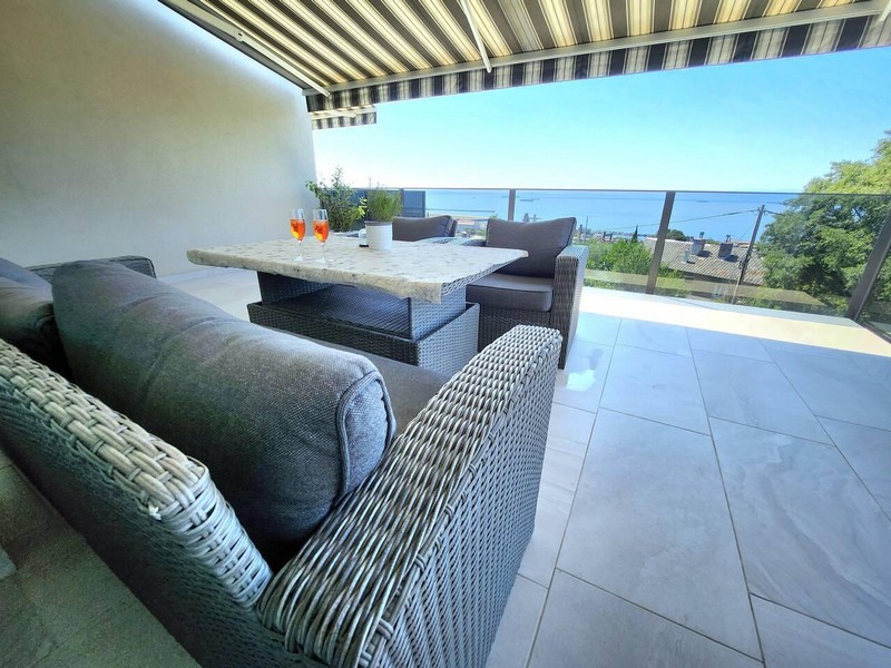 Terrazza coperta con divano in rattan, tavolo da pranzo e vista mare