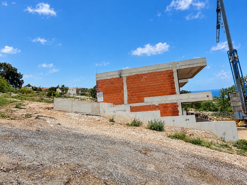 Costruzione al grezzo in mattoni con muro in cemento e gru su strada di ghiaia