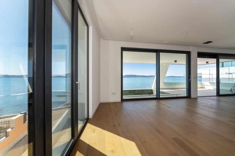 Zona giorno con pavimento in legno e finestre a tutta altezza con vista mare