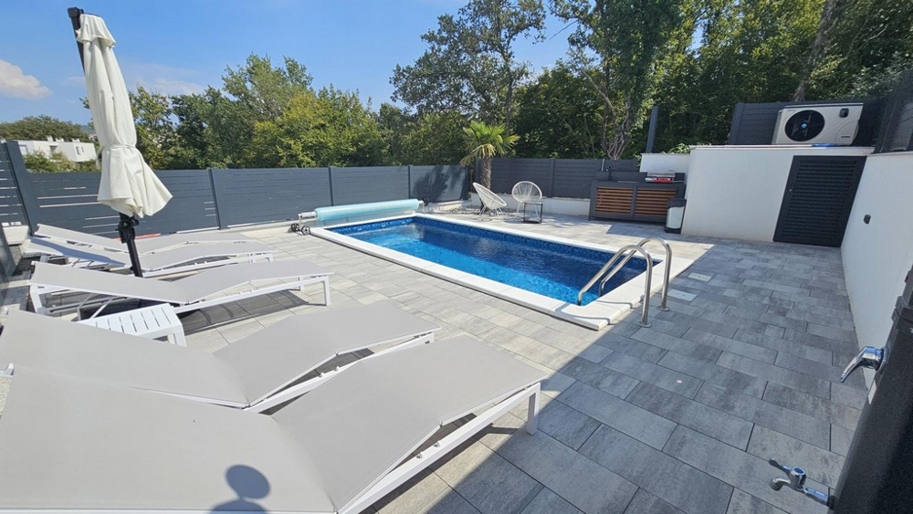 Giardino con piscina riscaldata e lettini dell'appartamento a Malinska