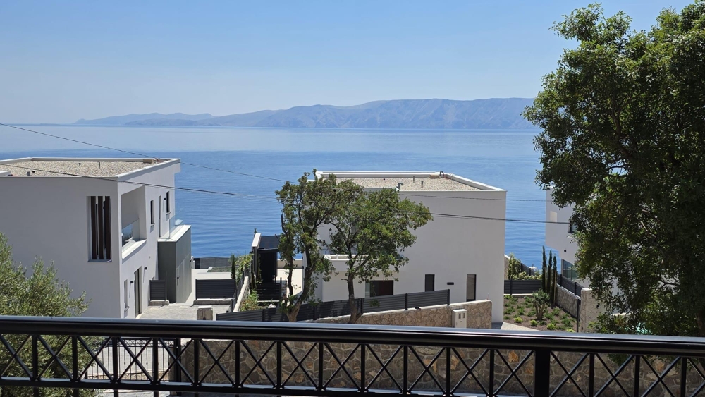 Vista dal balcone tra case bianche sul mare e sui monti