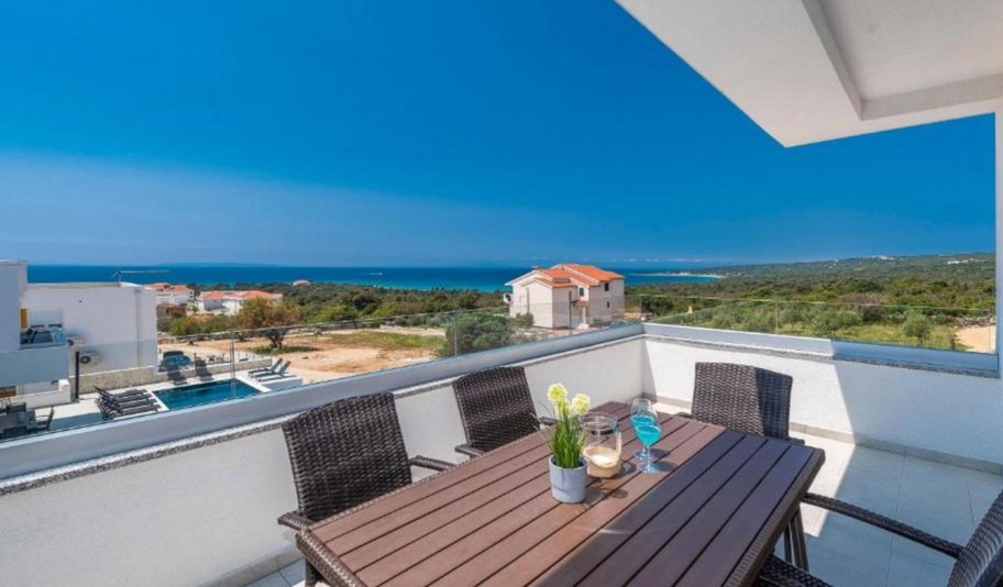 Tavolo sul balcone con sedie in vimini e vista su piscina e costa