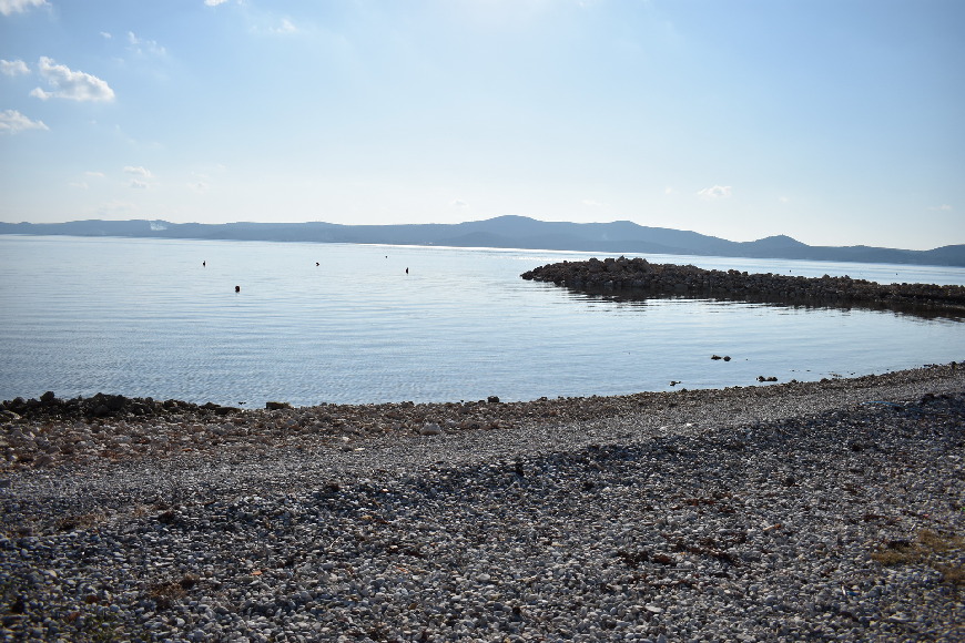 Spiaggia di ghiaia con molo di pietra e colline all'orizzonte