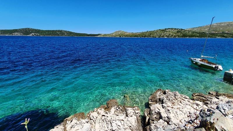Acqua turchese con barca a vela davanti alla riva rocciosa