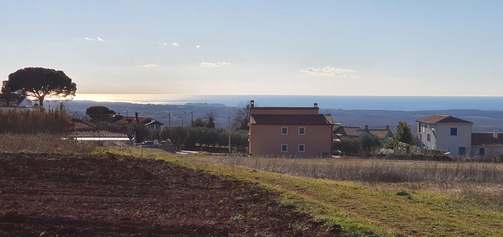 Campo arato con case e mare all'orizzonte
