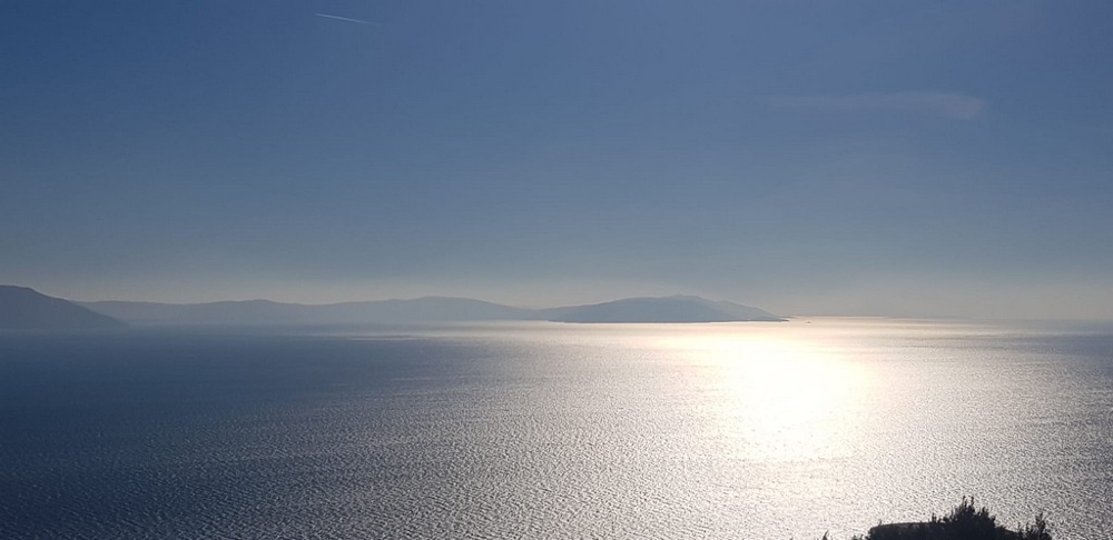 Riflesso del sole sul mare con sagome di isole nella foschia