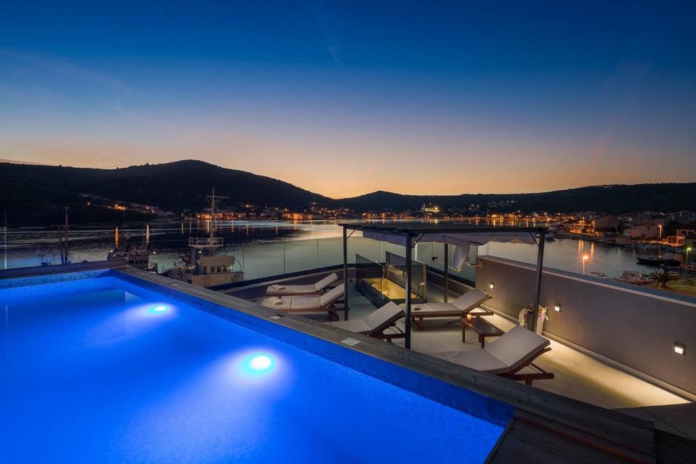 Piscina illuminata con lettini sopra il porto alla sera