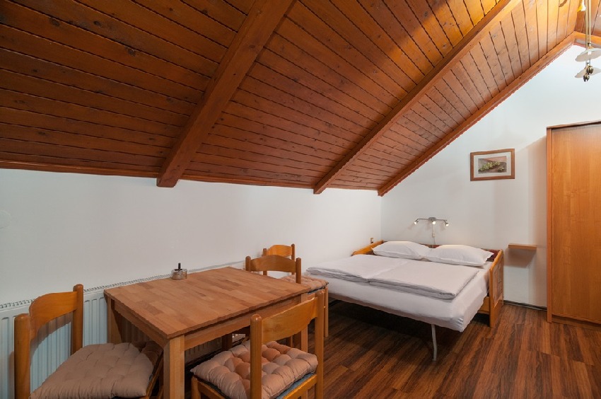 Stanza sottotetto con soffitto in legno, letto matrimoniale e tavolo da pranzo
