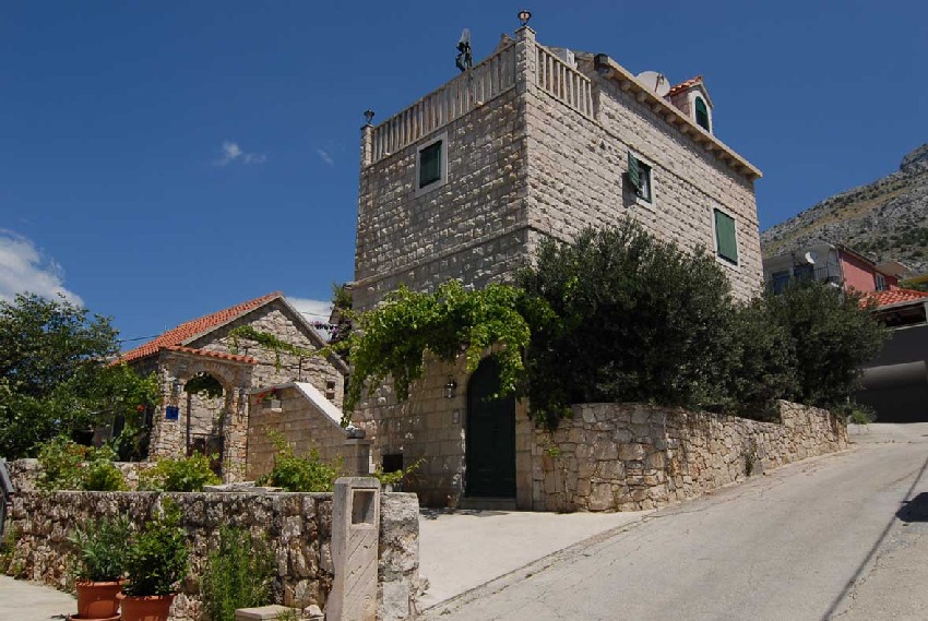 Casa in pietra con persiane verdi e pergolato di vite lungo la strada