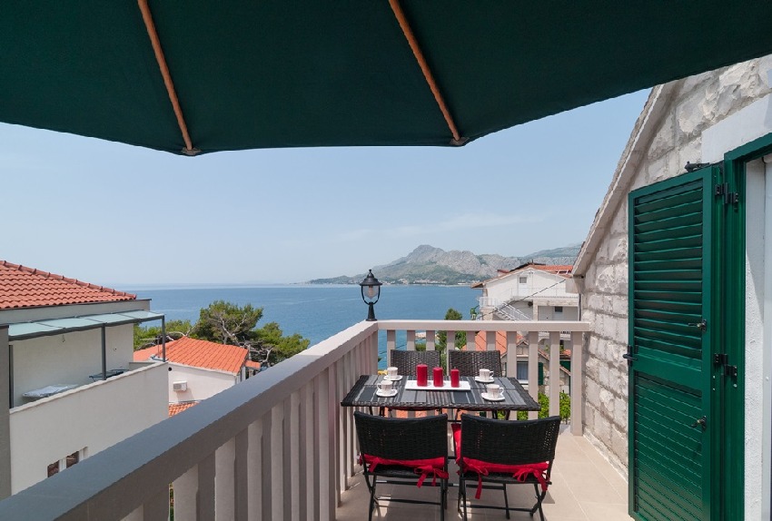 Balcone sotto un ombrellone verde con vista sulla baia e sui monti