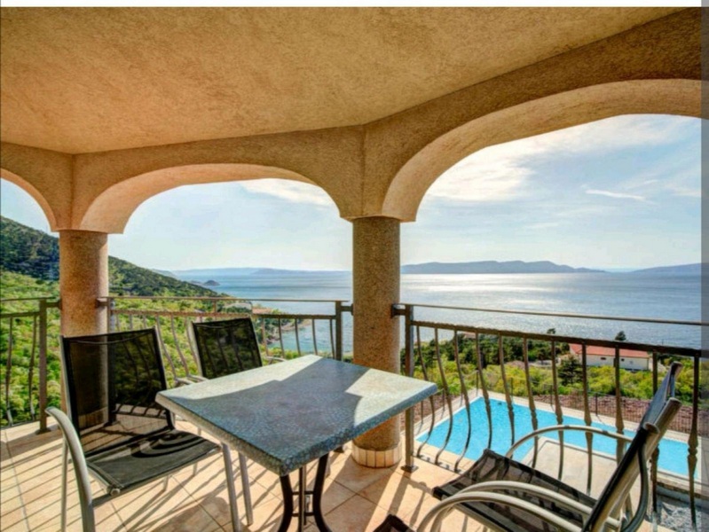Loggia con archi e tavolo in pietra sopra piscina e baia