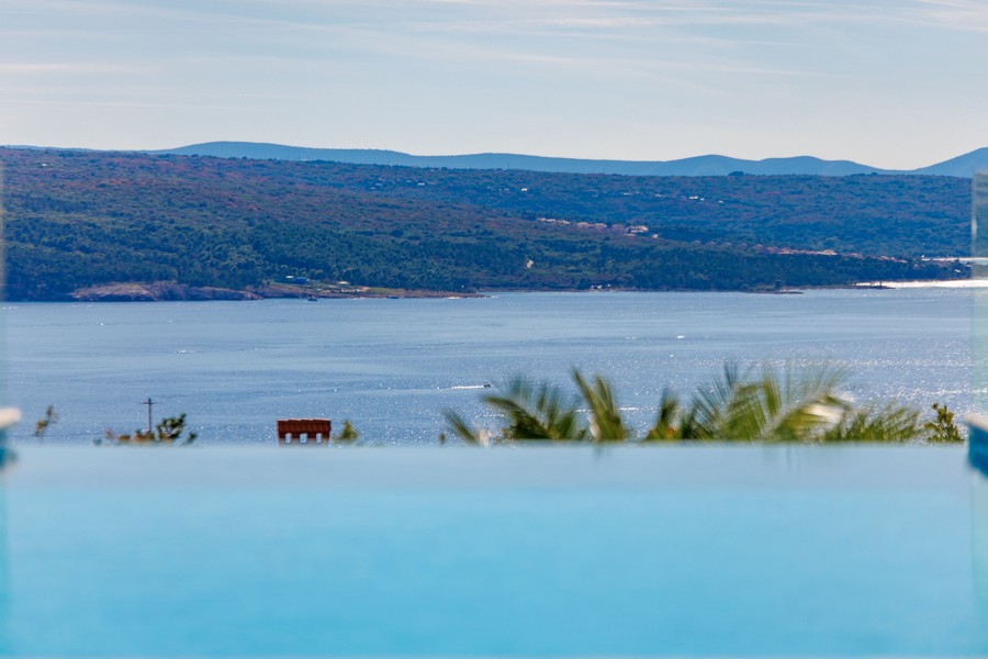 Zona pranzo coperta con griglia barbecue e vista su piscina e mare.