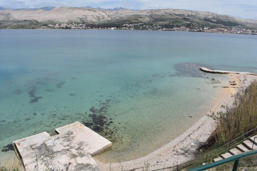 Baia poco profonda con spiaggia di ghiaia e pontile in cemento sull'isola di Pag