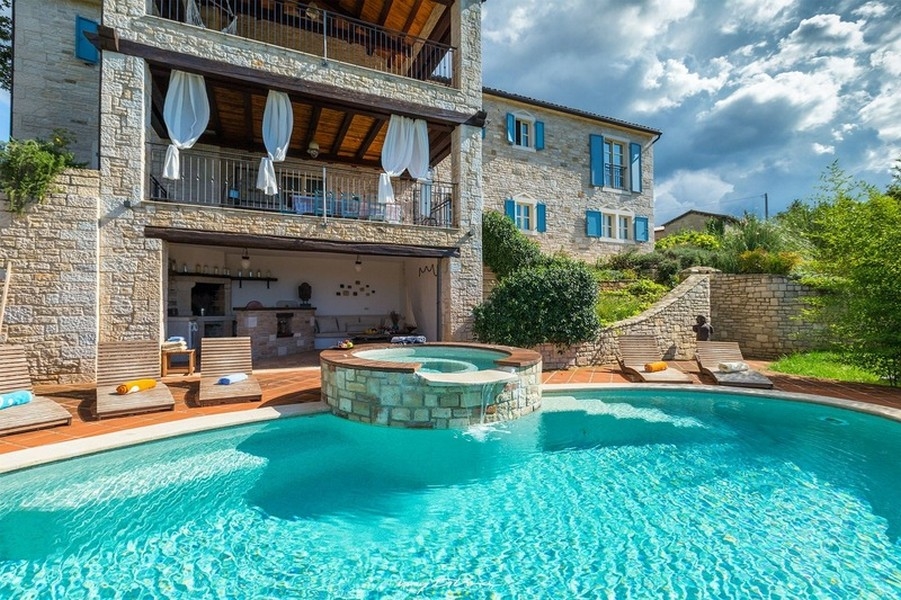Piscina con idromassaggio davanti alla casa in pietra con persiane blu