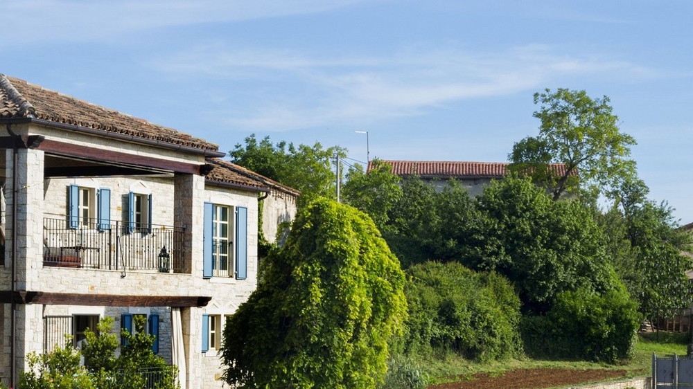 Casa in pietra con persiane blu e balcone dietro gli alberi
