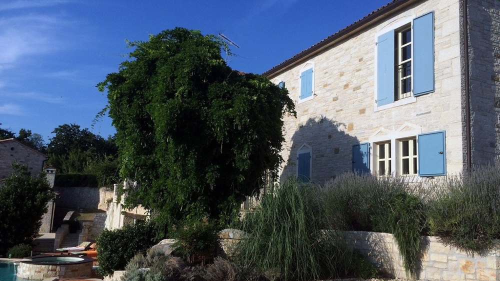 Facciata in pietra naturale con persiane blu sopra il giardino