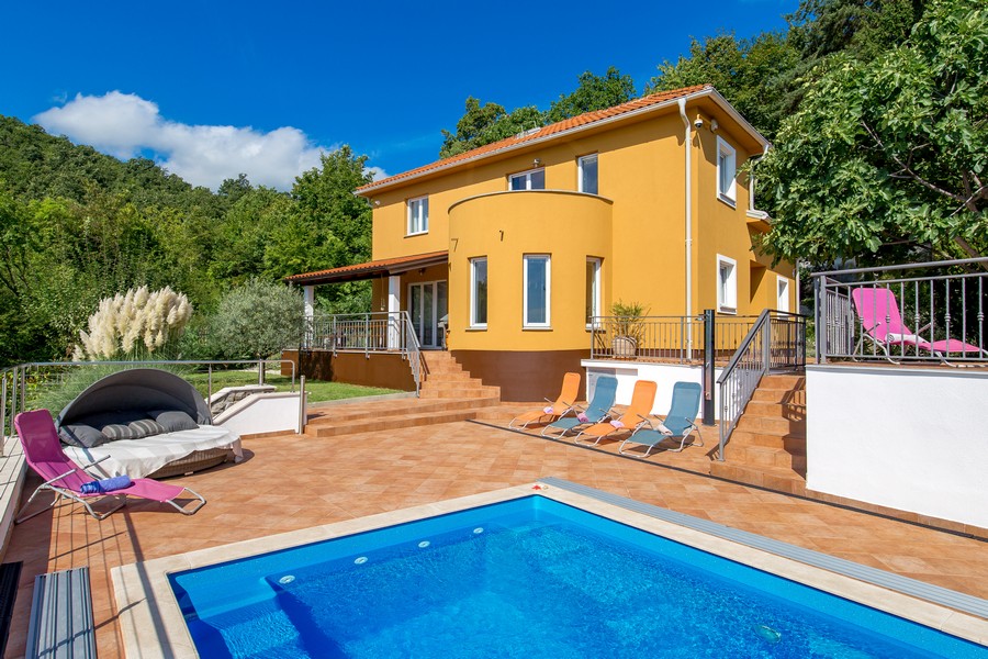 Villa gialla con corpo circolare e lettini a bordo piscina