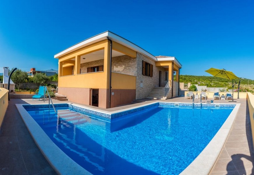 Grande piscina davanti alla casa con pietra naturale e ombrellone