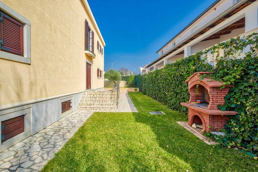 Striscia di prato accanto alla casa con barbecue in muratura alla siepe