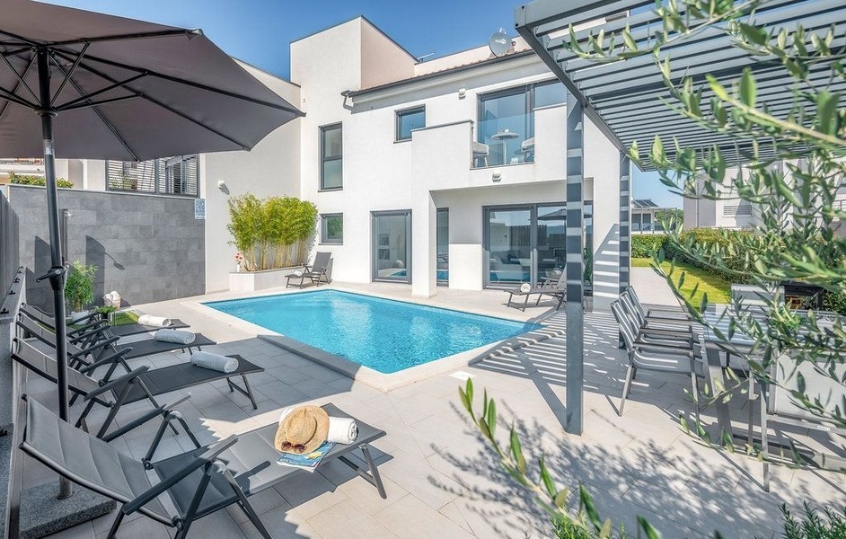 Piscina con ombrellone e lettini tra rami di ulivo