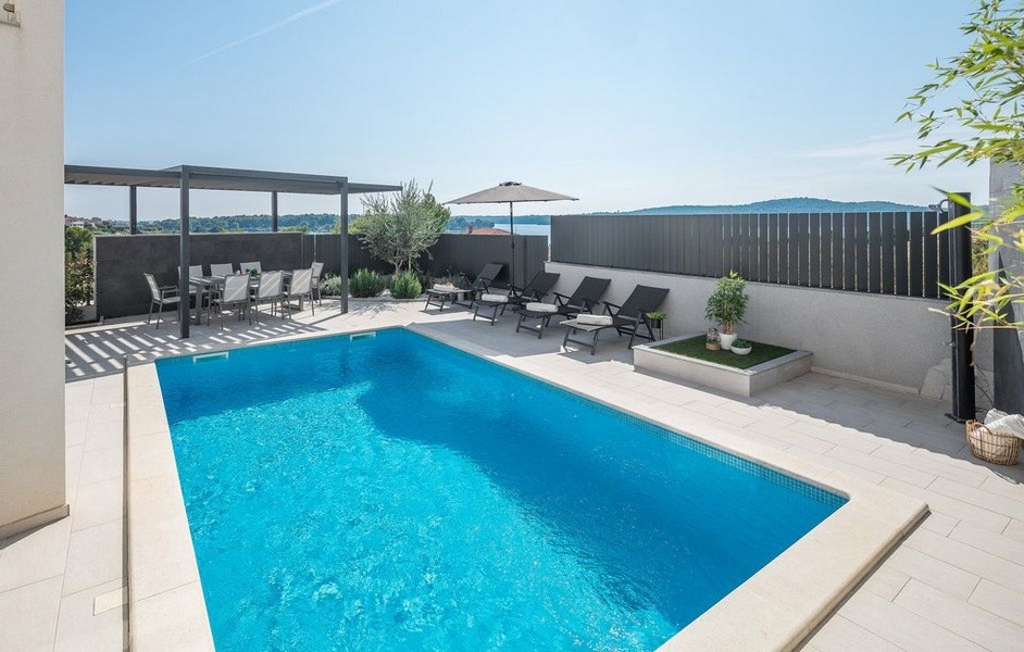 Piscina con lettini e pergola dietro il muro scuro