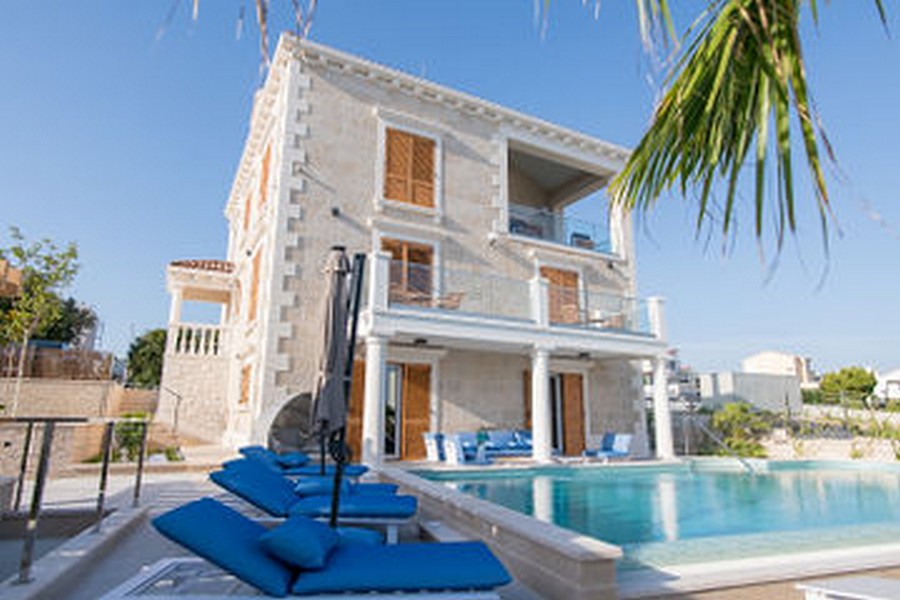Villa in pietra naturale chiara con piscina e lettini blu
