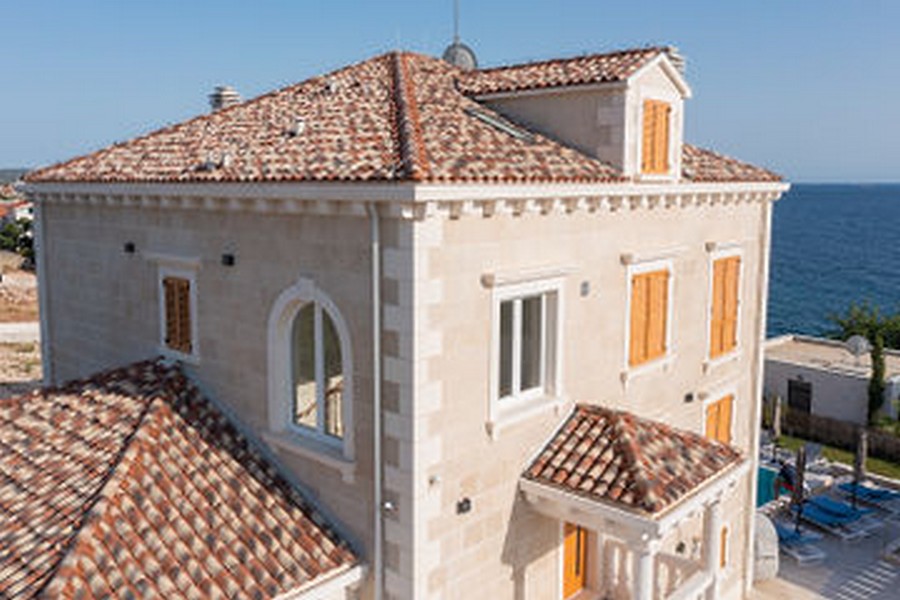 Villa in pietra con tetto di tegole e persiane in legno sul mare
