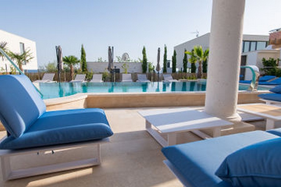 Mobili lounge blu a bordo piscina con cipressi dietro