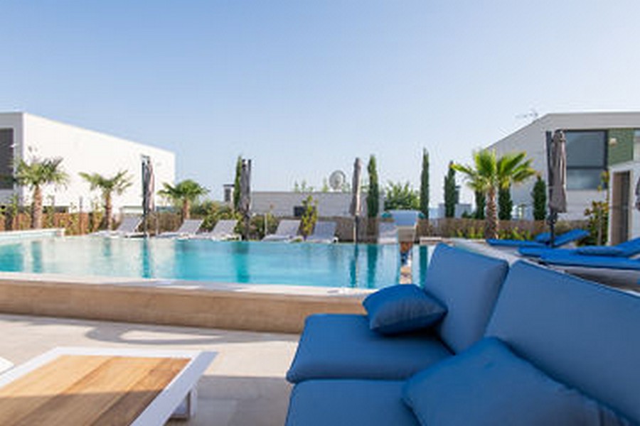 Area piscina con palme e divano blu in primo piano